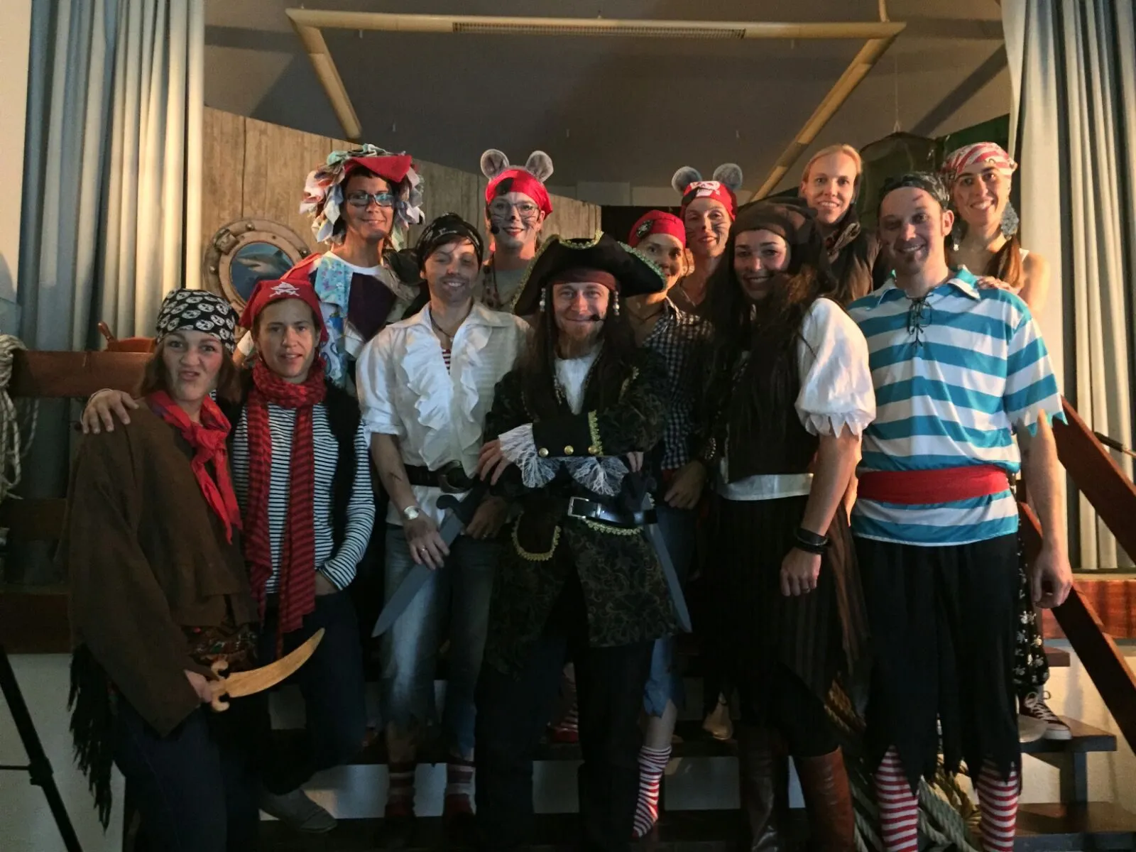 Gruppenfoto des Ensembles von „Der Schatz des Käpt'n Klaas“ in Kostüm — Piraten und Piratenbraut, Käpt'n Klaas mit Dreispitz in der Mitte und zwei Mäuse mit Öhrchen auf einer Schiffstreppe.