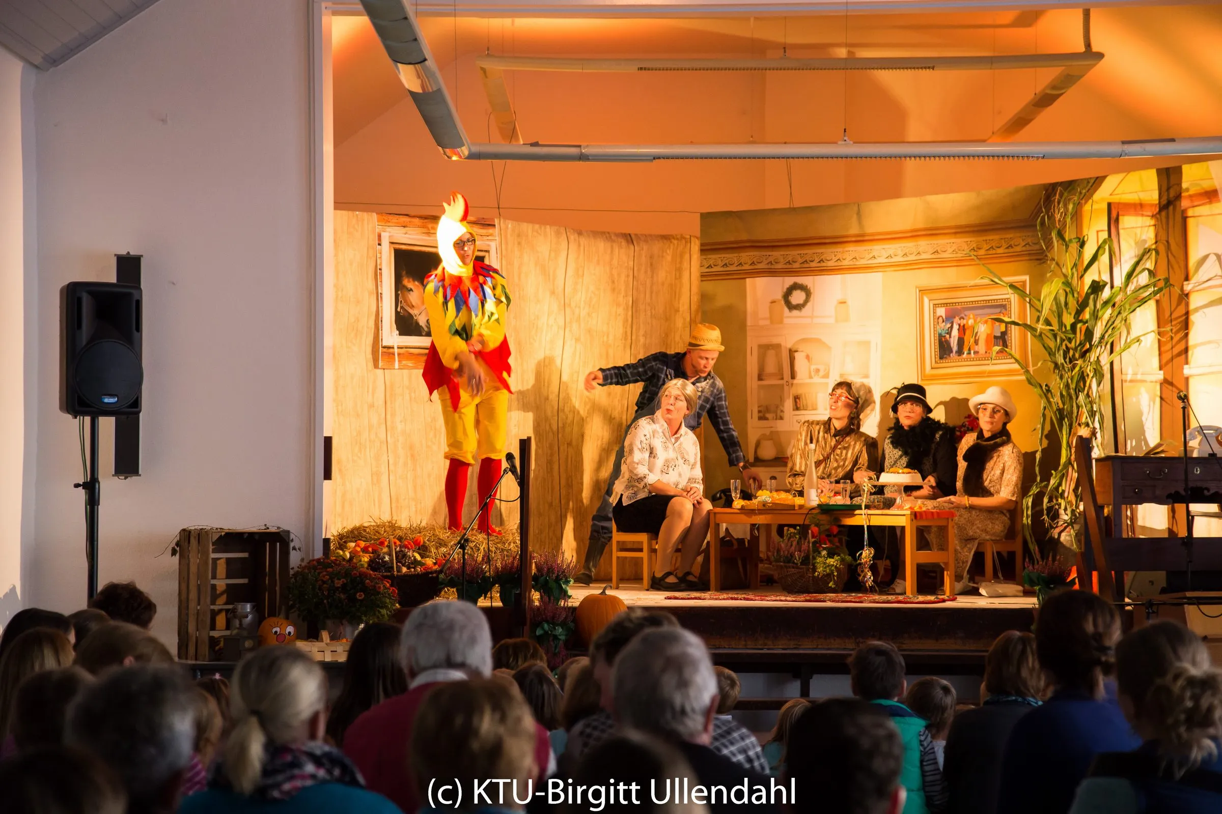 Hahn, Huhn und Kuh im Kostüm neben Bauer Anton und der am Tisch sitzenden Damenrunde.