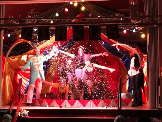 Das Ensemble jubelt unter dem Schriftzug „Zirkus“ in Konfettiregen vor der bunten Zirkuszelt-Kulisse.
