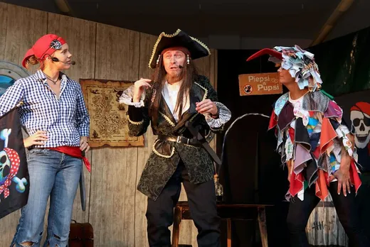 Käpt'n Klaas im Gespräch mit zwei weiteren Piratenfiguren vor der Bühnenkulisse, im Hintergrund eine Schatzkarte und das Schild „Piepsi & Pupsi".